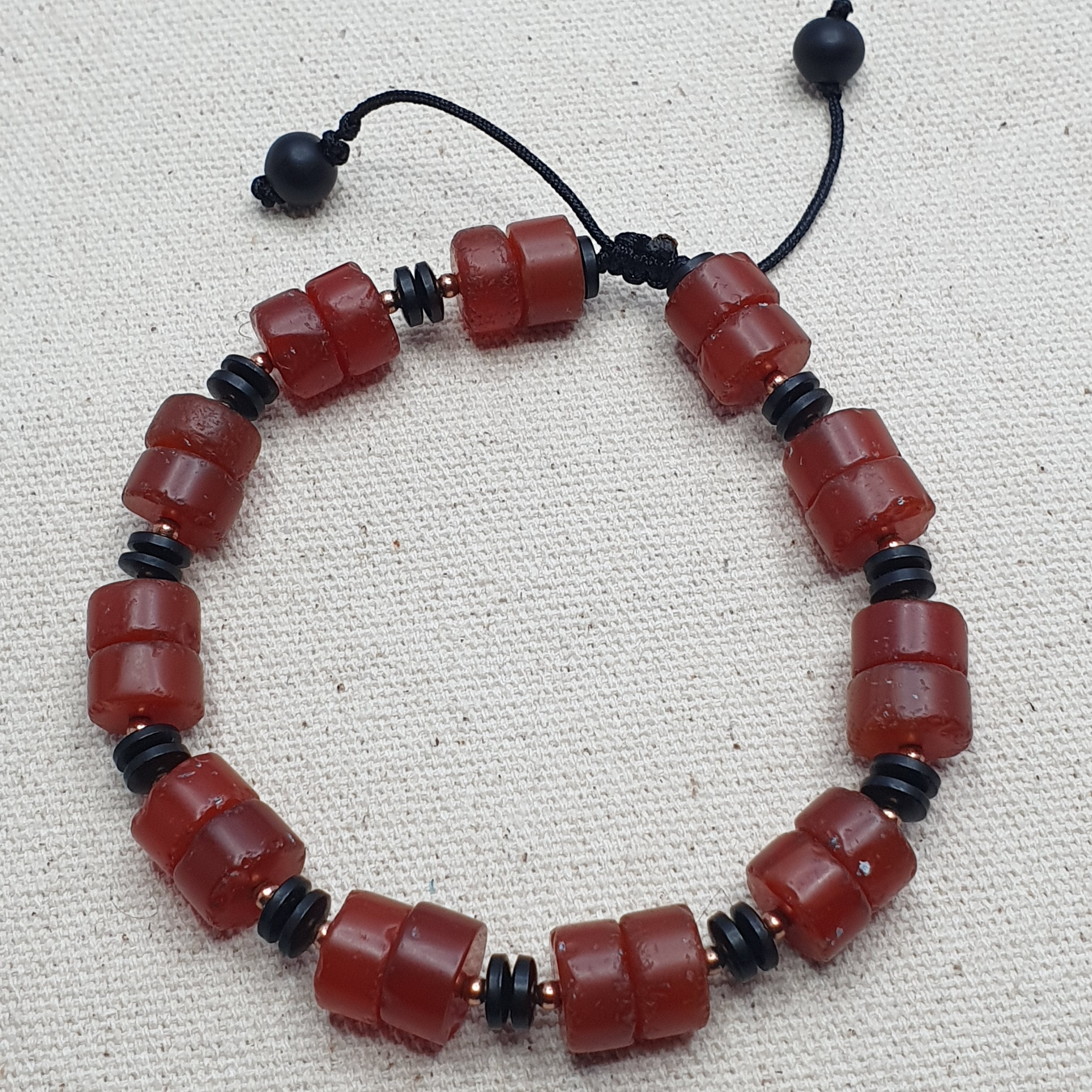 Carnelian Agate Beaded bracelet with red and black beads on a beige fabric background