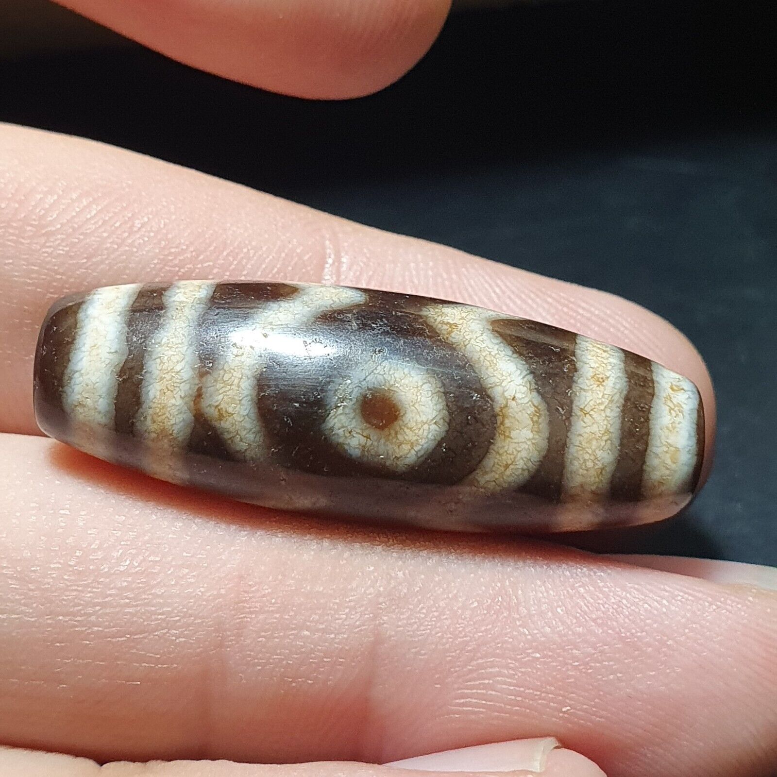 "Image of a vintage Tibetan Dzi amulet, featuring a rare and unique 3-eyed agate stone bead with an intricate pattern, believed to possess spiritual powers and bring protection and good fortune in Tibetan Buddhism."