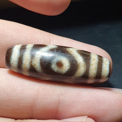 "Image of a vintage Tibetan Dzi amulet, featuring a rare and unique 3-eyed agate stone bead with an intricate pattern, believed to possess spiritual powers and bring protection and good fortune in Tibetan Buddhism."